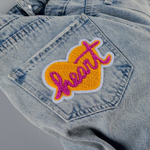 Chenille Heart Shaped Patch with the word heart in the center applied to jeans