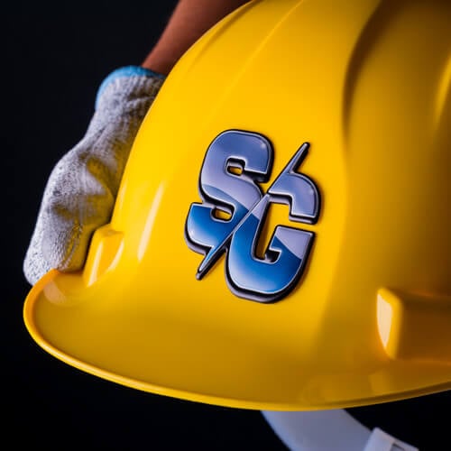 Man's hand in a glove holding a yellow safety helmet with a FlexStyle Domed SC emblem