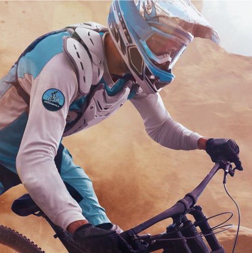 Close up of a dirt biker riding his bike with dust kicked up into the air, wearing a protective shirt with a Sublimated bike patch on his upper arm